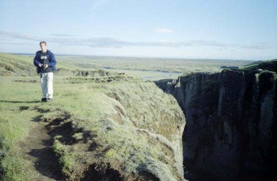 Dave standing by the gorge with a view to the sea across the lava fields in the background